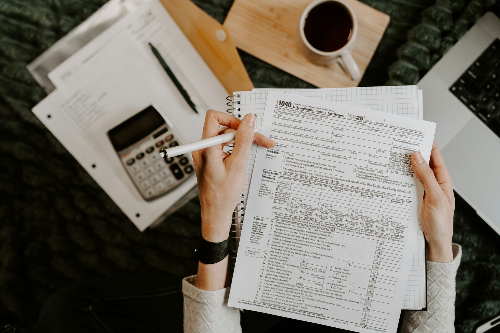 Hands reviewing a paper form with a laptop and calculator on the desk